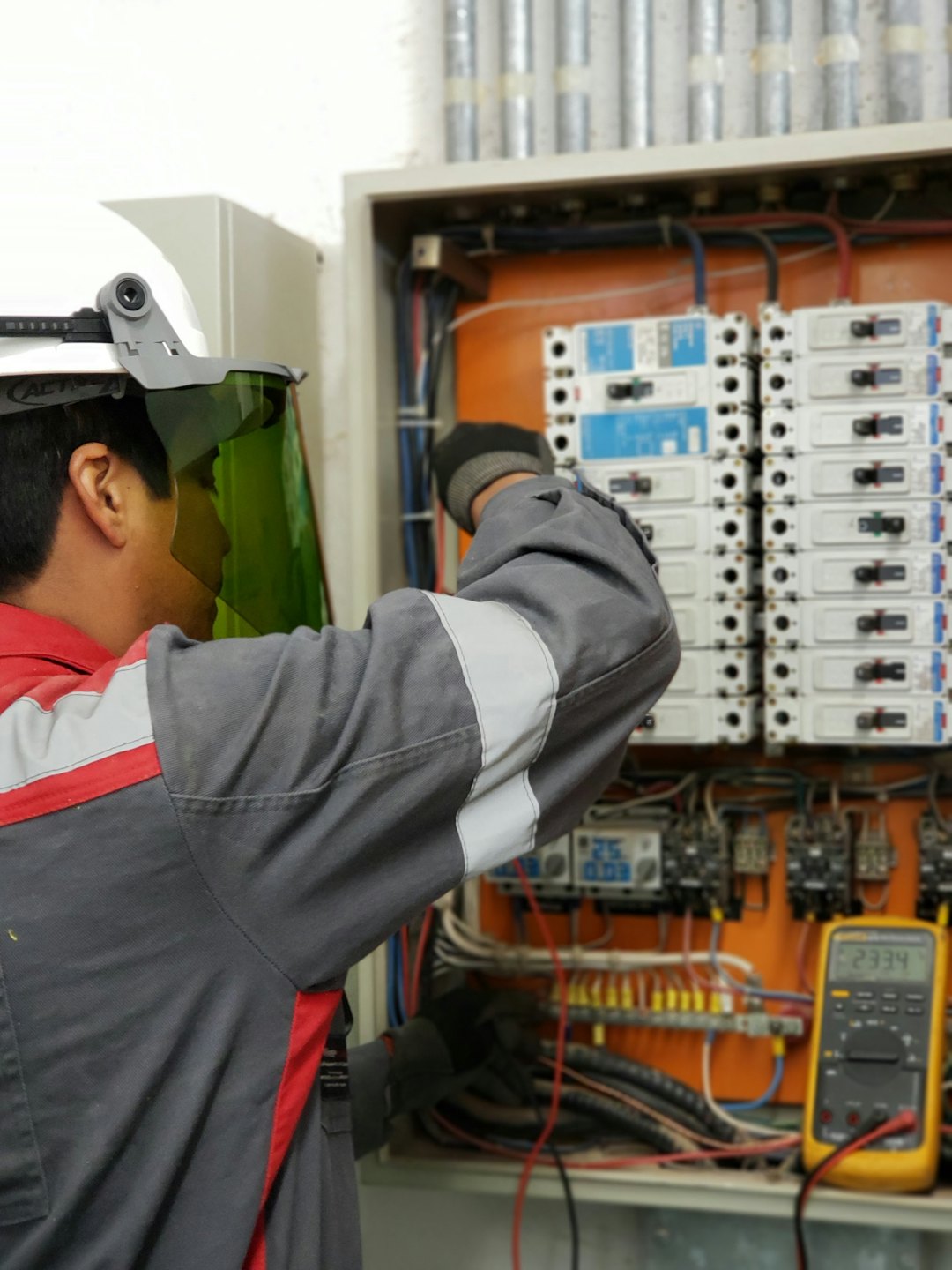 Techniker inspiziert offenen Elektroschaltkasten mit Sicherungen und Verkabelung.